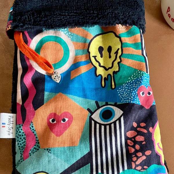 Gant de soins farfelu Paddy Style posé sur une table, avec motifs colorés et face en éponge noire, conçu pour le soin des animaux.